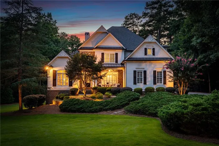 Traditional white siding residence featuring dark shutters, a covered porch, multiple gables, and a mature landscaped lawn with established shrubbery