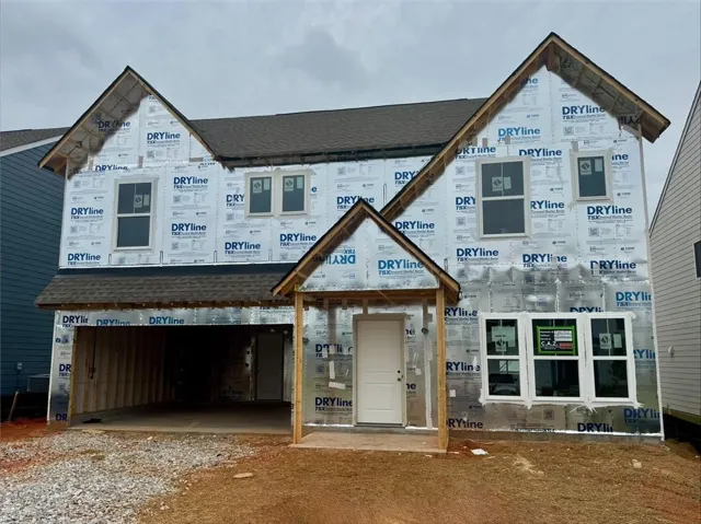 Two-story residential structure under construction featuring a dark shingled roof, multiple windows with white frames, and a prominent front entry door