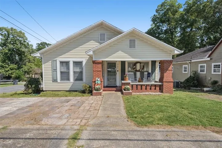 Siding exterior with a covered front porch, brick columns, and a concrete driveway with brick paver accents