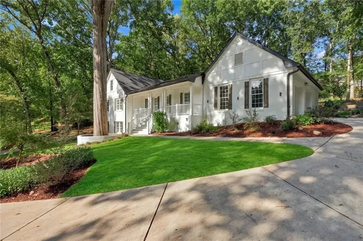White exterior with dark roof, a concrete driveway, manicured lawn, and natural landscaping