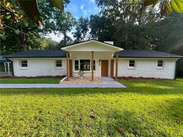 White painted brick exterior with dark shingle roofing, featuring a covered entry with wood support columns