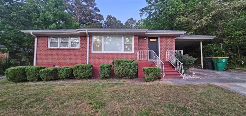 Brick exterior with a covered carport, front entry with painted stairs and white railings, and mature landscaping