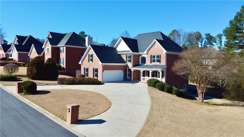 Brick facade home featuring a two-car garage, covered entry porch, and a large paved driveway