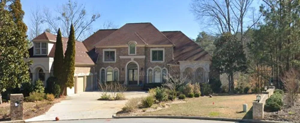 Brick facade residence featuring a prominent arched entry, multiple gables, an attached two-car garage, mature landscaping, and an extended paved driveway