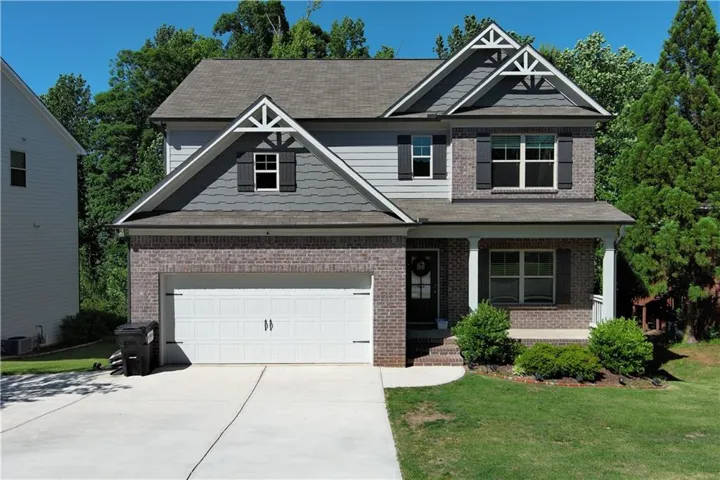 Two-story residence featuring a brick and siding facade, a two-car garage, covered front porch, and decorative gable accents