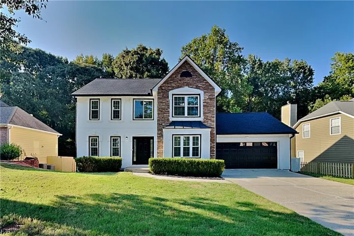 Two-story residence featuring a combination of white siding and stone veneer, a dark shingle roof, and an attached two-car garage with a dark door