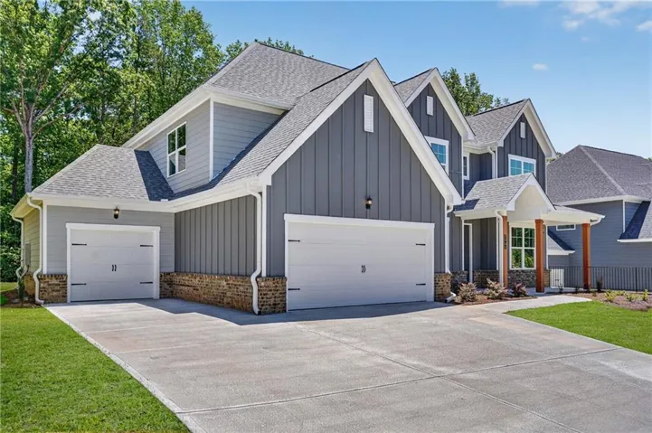 Modern farmhouse exterior featuring gray siding, white trim, a multi-car driveway, and a covered porch with stone and wood accents