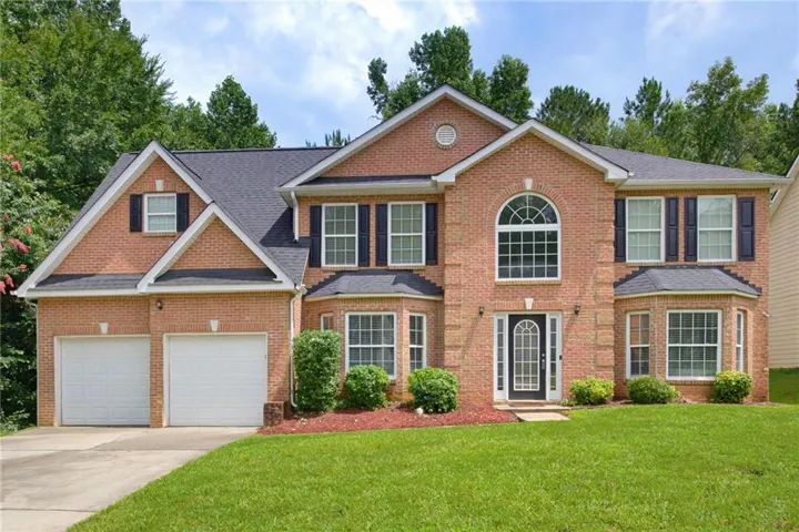 Traditional brick exterior featuring a two-car garage, arched window, bay window, dark shutters, and a dark shingle roof