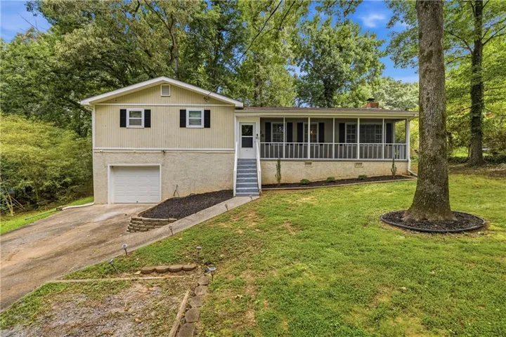 Split-level residence featuring a one-car garage, screened front porch with white railing, and a stone retaining wall