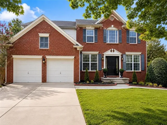Brick exterior with white trim, two-car garage, concrete driveway, and landscaped front yard with a stone walkway
