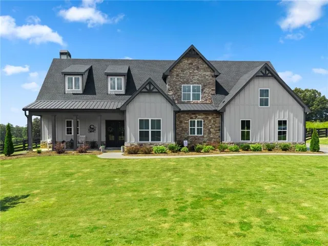 Board and batten siding with stone accents, covered front porch, dormer windows, and a black metal roof over the porch