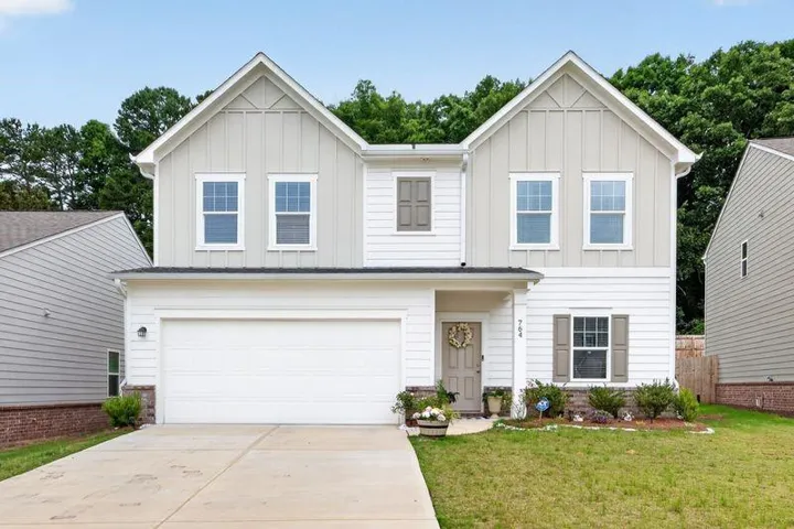 Two-story home with a two-car garage, white siding, light gray board-and-batten gables, and a concrete driveway