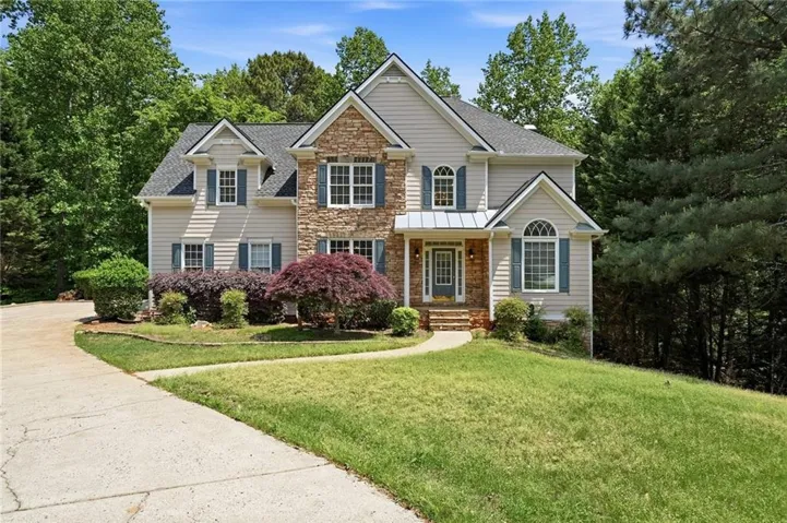 Two-story residence featuring stone and siding exterior, blue window shutters, dormer windows, a covered entryway, and a sloped front lawn