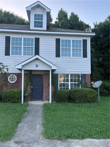 Two-story exterior featuring a dormer window, white siding, black shutters, brick accents, and a covered entry