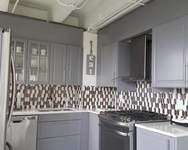 Kitchen with appliances with stainless steel finishes, wall chimney exhaust hood, gray cabinetry, backsplash, and light countertops