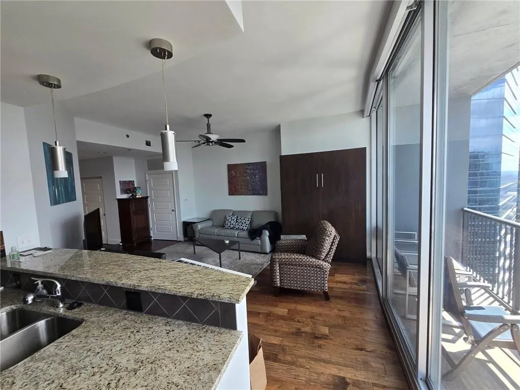 Kitchen featuring a ceiling fan, dark wood-style flooring, hanging light fixtures, and light stone counters