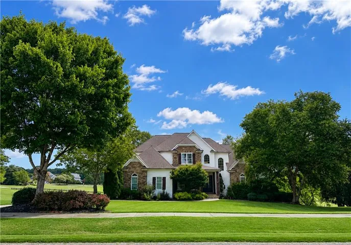 Two-story residence featuring a gabled roof, stone and siding exterior, arched windows, and mature trees