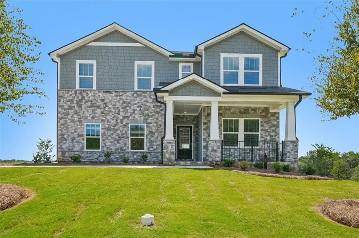 Two-story residence featuring a stone and shingle facade, covered entry porch with columns, a dark front door, and multiple windows