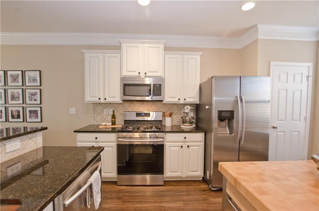 Kitchen with white cabinetry, dark hardwood / wood-style flooring, stainless steel appliances, and backsplash Kitchen with white cabinetry, dark hardwood / wood-style flooring, stainless steel appliances, and backsplash