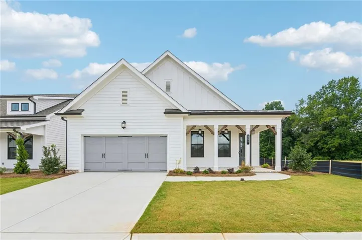 Modern farmhouse exterior featuring white horizontal siding, a covered front porch with exposed wood beams, a two-car garage with light gray doors, a concrete driveway, and a manicured lawn