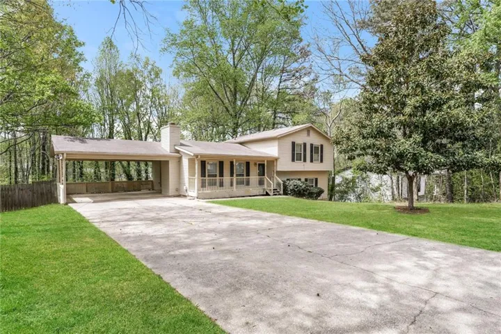 Tri-level home with a porch, a chimney, a front lawn, driveway, and an attached carport