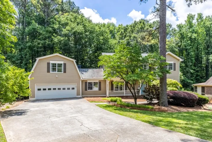 Siding exterior home featuring a two-car garage, concrete driveway, front porch with white railing, and mature landscaping