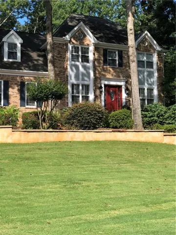 Traditional brick exterior with white trim, a striking red entry door, and dormer windows