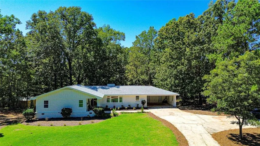 White brick and siding exterior with a light gray shingle roof, a two-car carport, a paved driveway, and mature landscaping