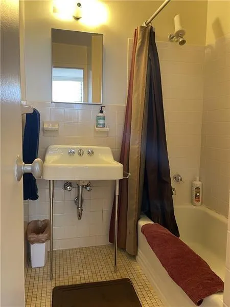 Bathroom featuring tile floors, shower / bath combo, tile walls, and sink
