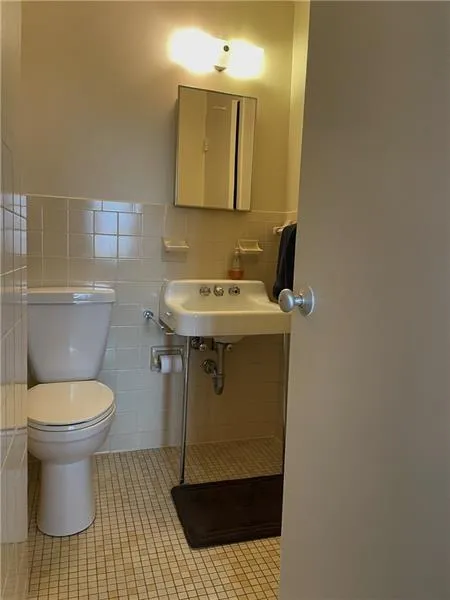 Bathroom featuring toilet, sink, tile floors, backsplash, and tile walls