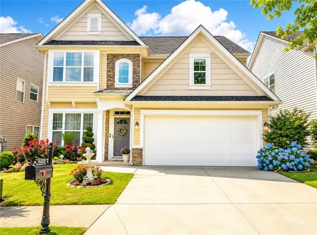 Two-story residence featuring light yellow siding, stone accents, a dual-door garage, and a gabled roofline