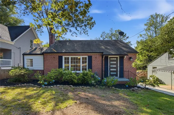 Brick exterior with a dark-shingle roof, featuring a multi-pane window with dark shutters, a modern entry door, and a front porch with an iron railing