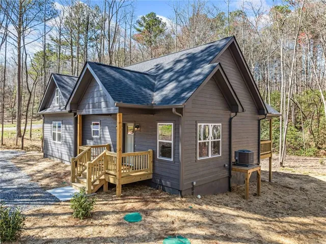 Charming cottage-style home featuring a gabled roof with dark asphalt shingles, horizontal siding exterior, and a covered front porch with wooden railings