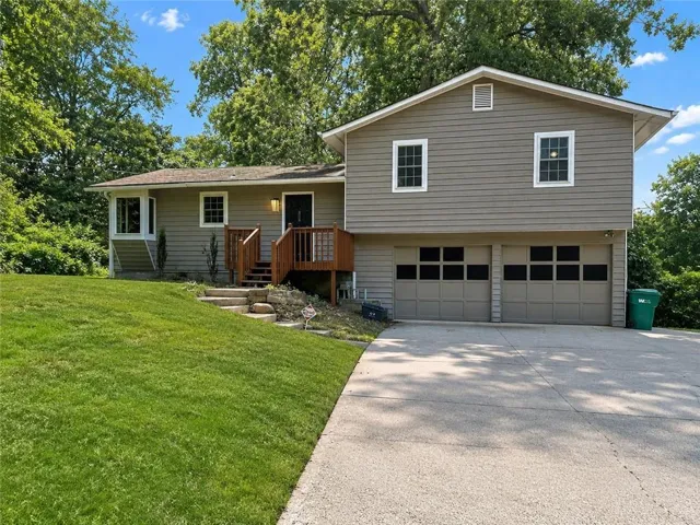 Split-level residence featuring siding exterior, an attached two-car garage, a concrete driveway, and a wood-decked entryway with stairs