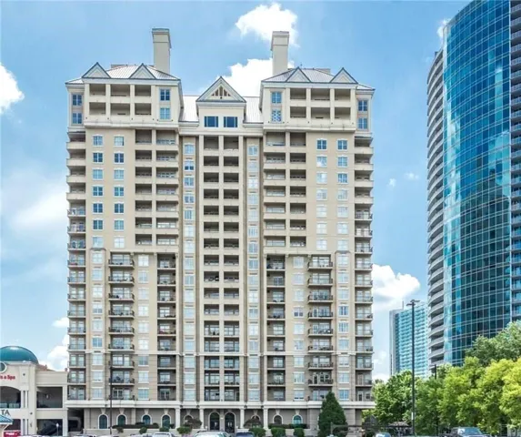 Multi-story building featuring numerous private balconies, arched ground-level windows, a central gable roofline, and distinctive rooftop dormers
