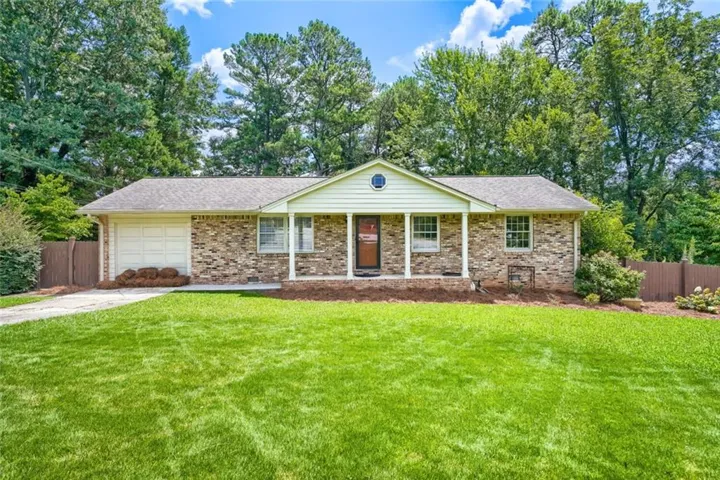 Brick facade home featuring a covered front porch with white columns, an attached garage, and a lush lawn