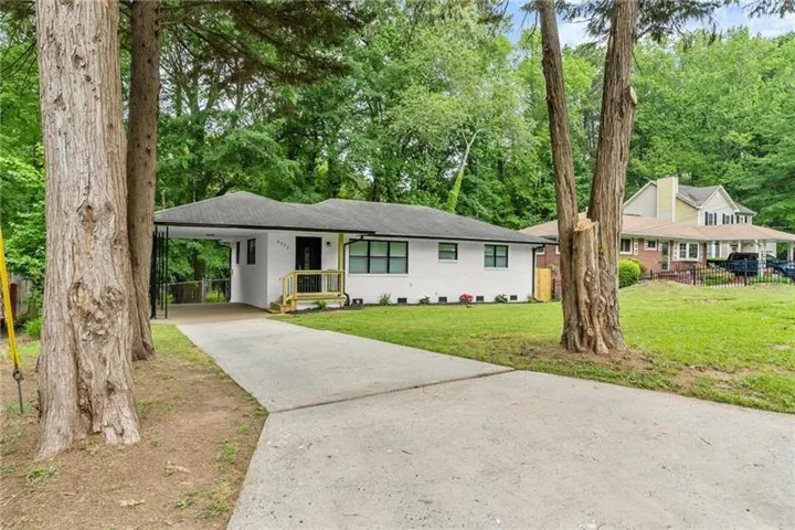 White exterior with dark trim windows, covered carport, front entry porch with yellow railing, and a paved driveway