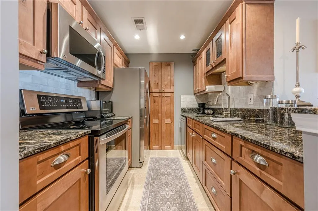 Kitchen featuring stainless steel appliances, tasteful backsplash, brown cabinets, dark stone counters, and recessed lighting