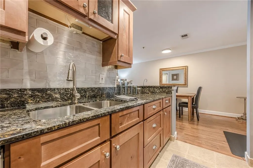 Kitchen with crown molding, backsplash, dark stone counters, brown cabinets, and glass insert cabinets