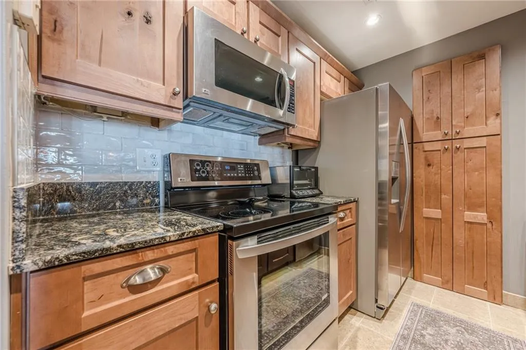 Kitchen with stainless steel appliances, tasteful backsplash, dark stone counters, and light tile patterned flooring