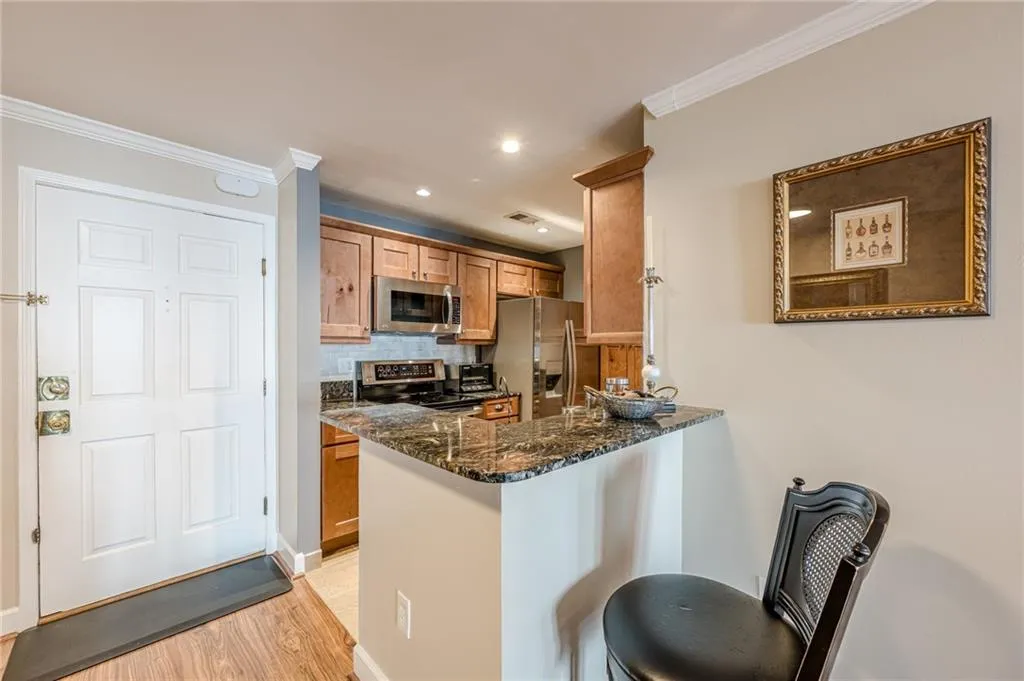 Kitchen with stainless steel appliances, light wood-style flooring, dark stone counters, ornamental molding, and backsplash