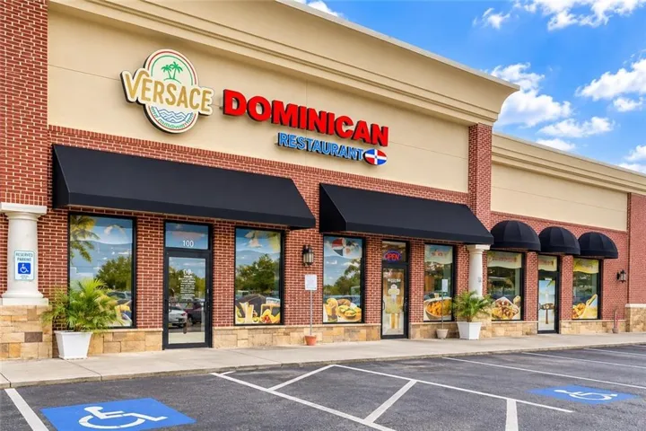Red brick facade with stone base, multiple storefront windows, black awnings, and an expansive parking area