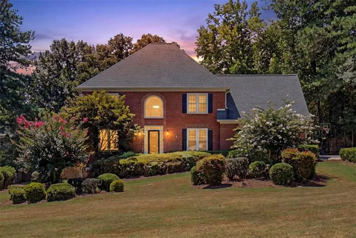 Brick Colonial estate showcasing a symmetrical façade with multiple gabled rooflines, arched entry, and illuminated windows