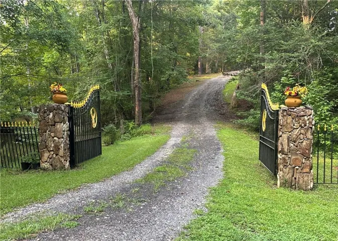 Gated entry with stone pillars, ornate black and gold metal gates, and a gravel driveway