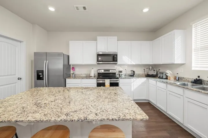 Kitchen island featuring a spacious countertop, white shaker-style cabinetry, stainless steel appliances, wood-finish flooring, and a double basin sink