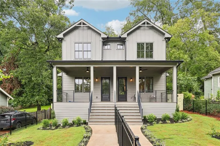 Modern farmhouse-style duplex featuring light gray vertical and horizontal siding, covered front porches with black railings, black-framed windows, and a manicured lawn with a paved walkway