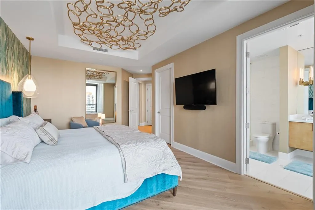 Bedroom featuring light wood finished floors, a tray ceiling, and ensuite bathroom