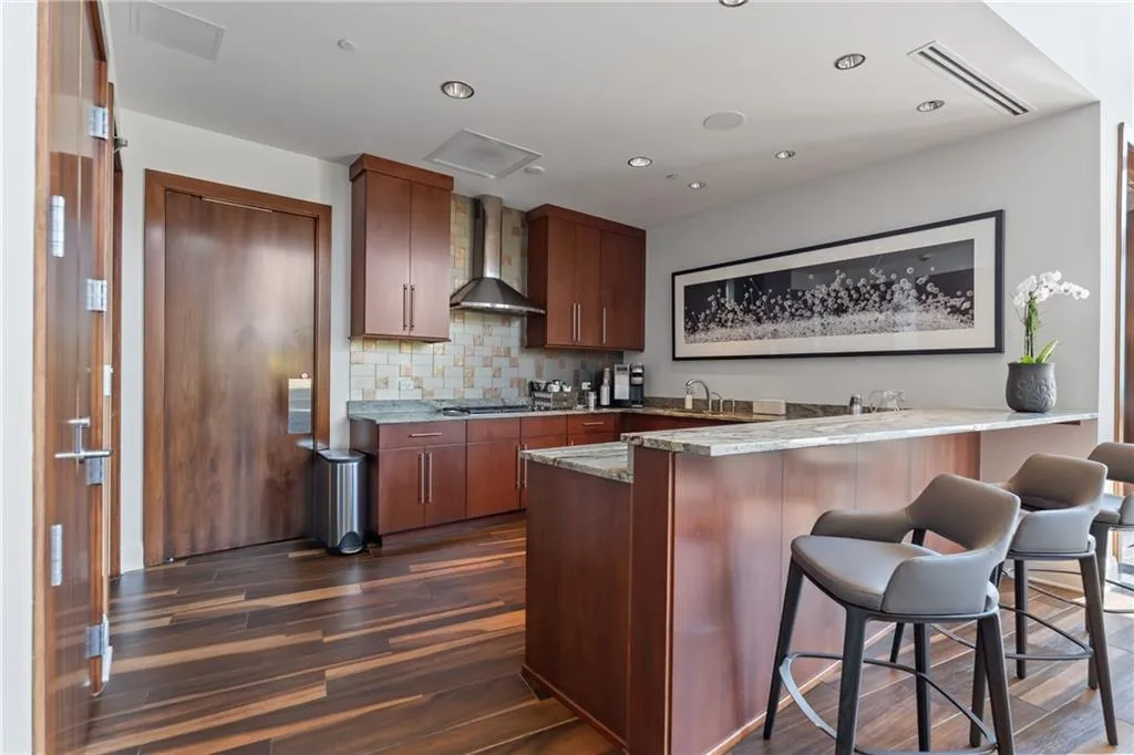 Kitchen with a peninsula, dark wood-style flooring, backsplash, a kitchen breakfast bar, and wall chimney range hood