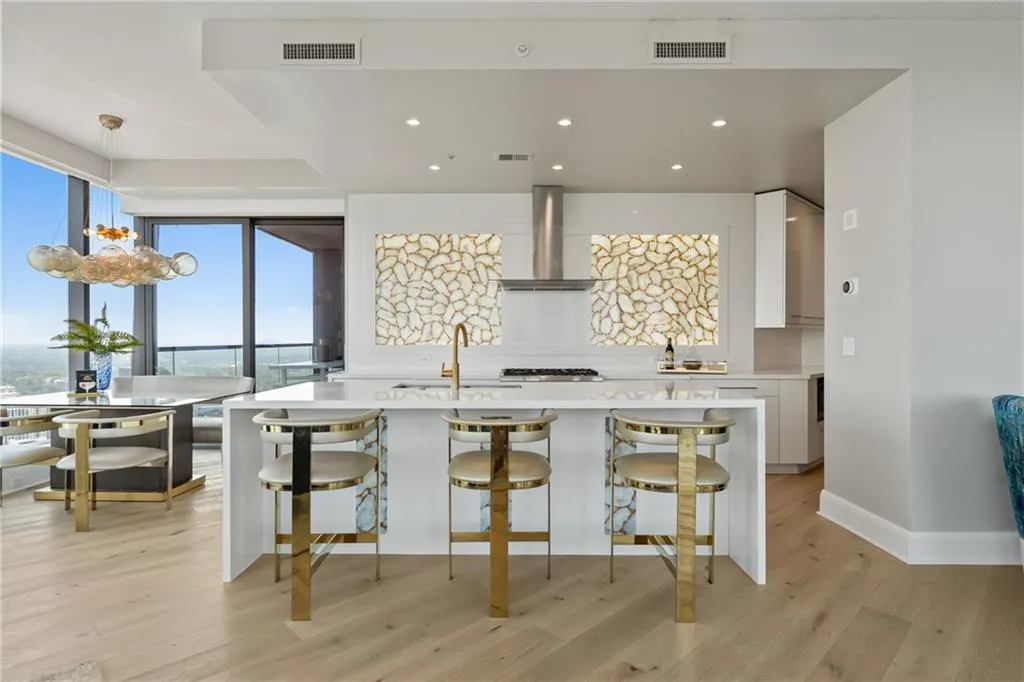 Kitchen with decorative light fixtures, light stone countertops, an island with sink, white cabinetry, and recessed lighting