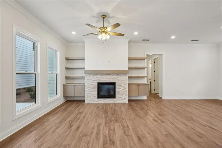 Spacious living area featuring wood-finish flooring, recessed lighting, and a prominent fireplace with a light-toned stone surround and wood mantel